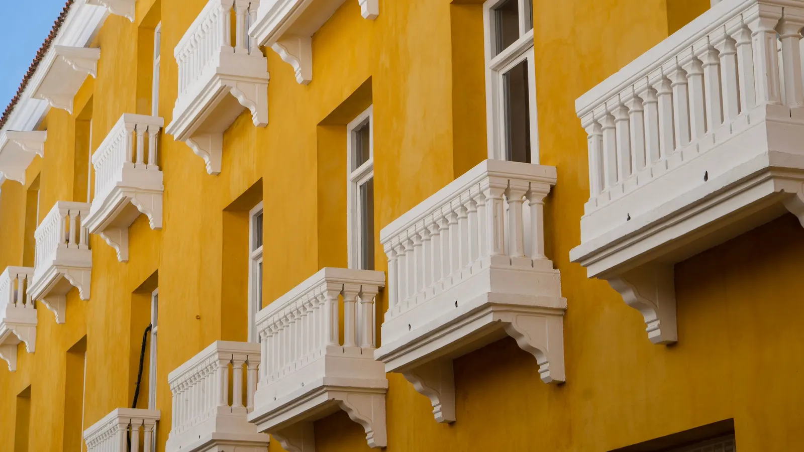 Fachada colonial amarilla en Cartagena con hileras de balcones blancos tallados bajo un cielo despejado
